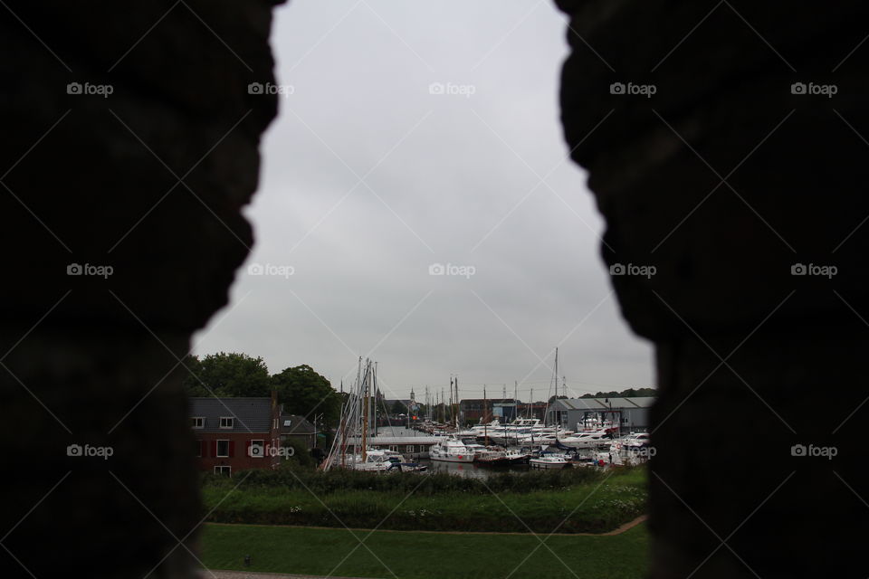 View of a European harbor through the walls of a brick fortress castle on a grey dreary summer day.