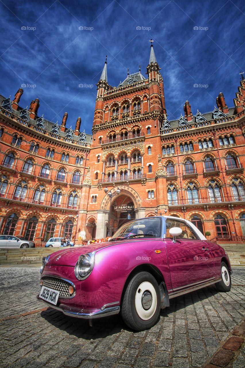 A classic, purple car parked in front of the grand architecture of The St Pancras hotel in London.