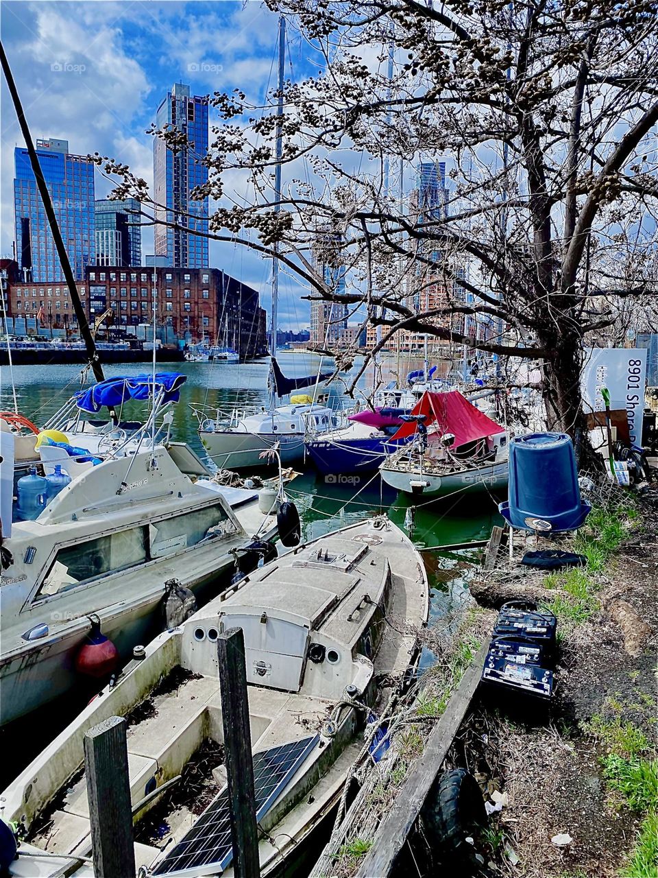 Different kinds of boats are tied to the shore here at “Newtown Creek” by the “Pulaski Bridge” in “Long Island City”, Queens and the ocean appears sleek, smooth and shiny today. 2023. Hypnotic Productions