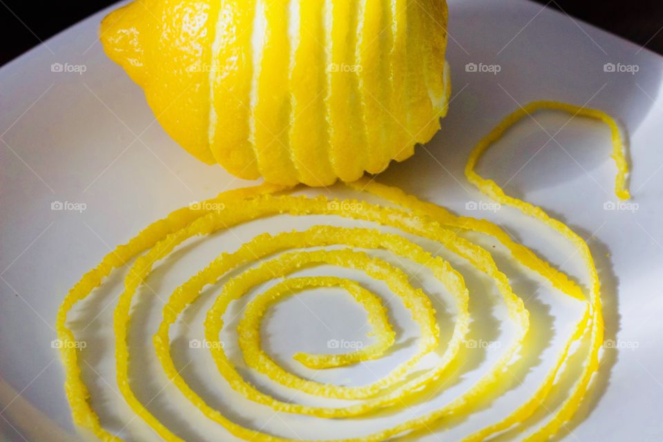 Lemon and spiraled lemon peel on a white plate with a dark background  