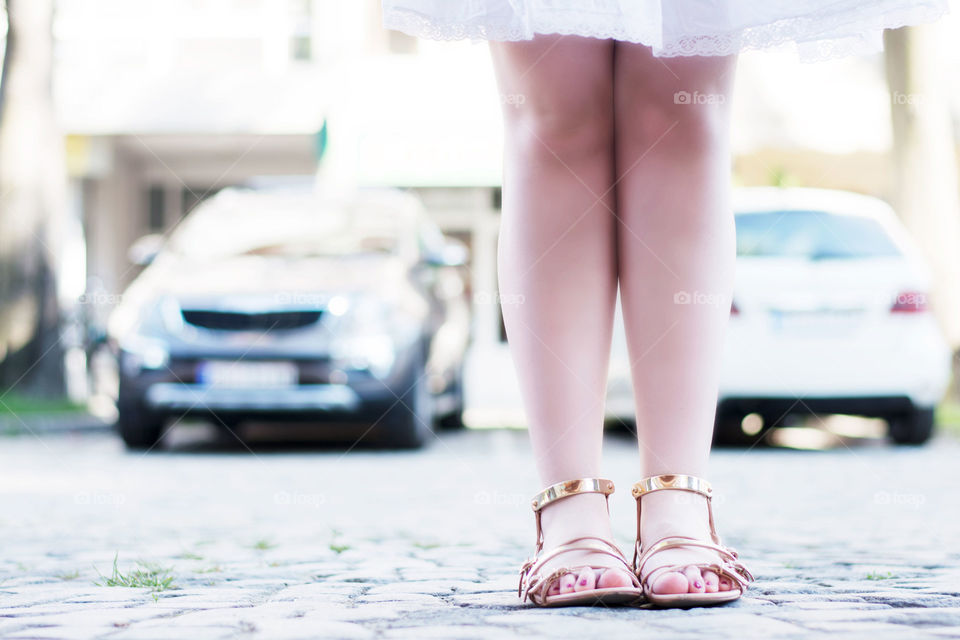 golden sandals. girl wearing white dress and golden sandals closeup of legs