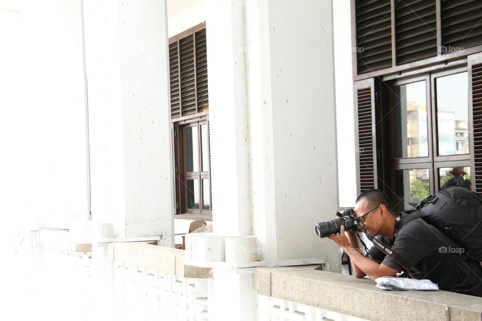 portrait of a man shooting a photo or video object from the top of a white-walled building.