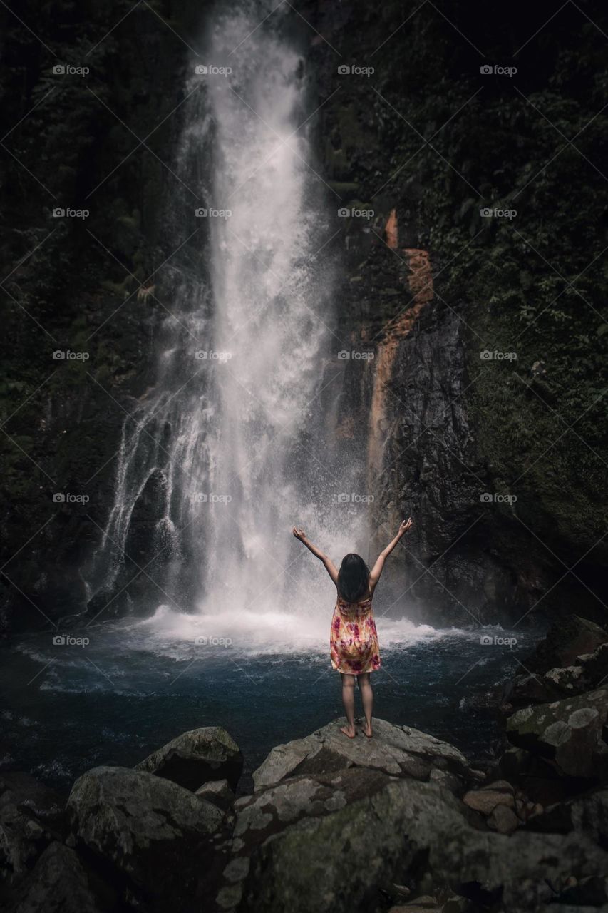 a woman is standing enjoying the waterfall breeze
