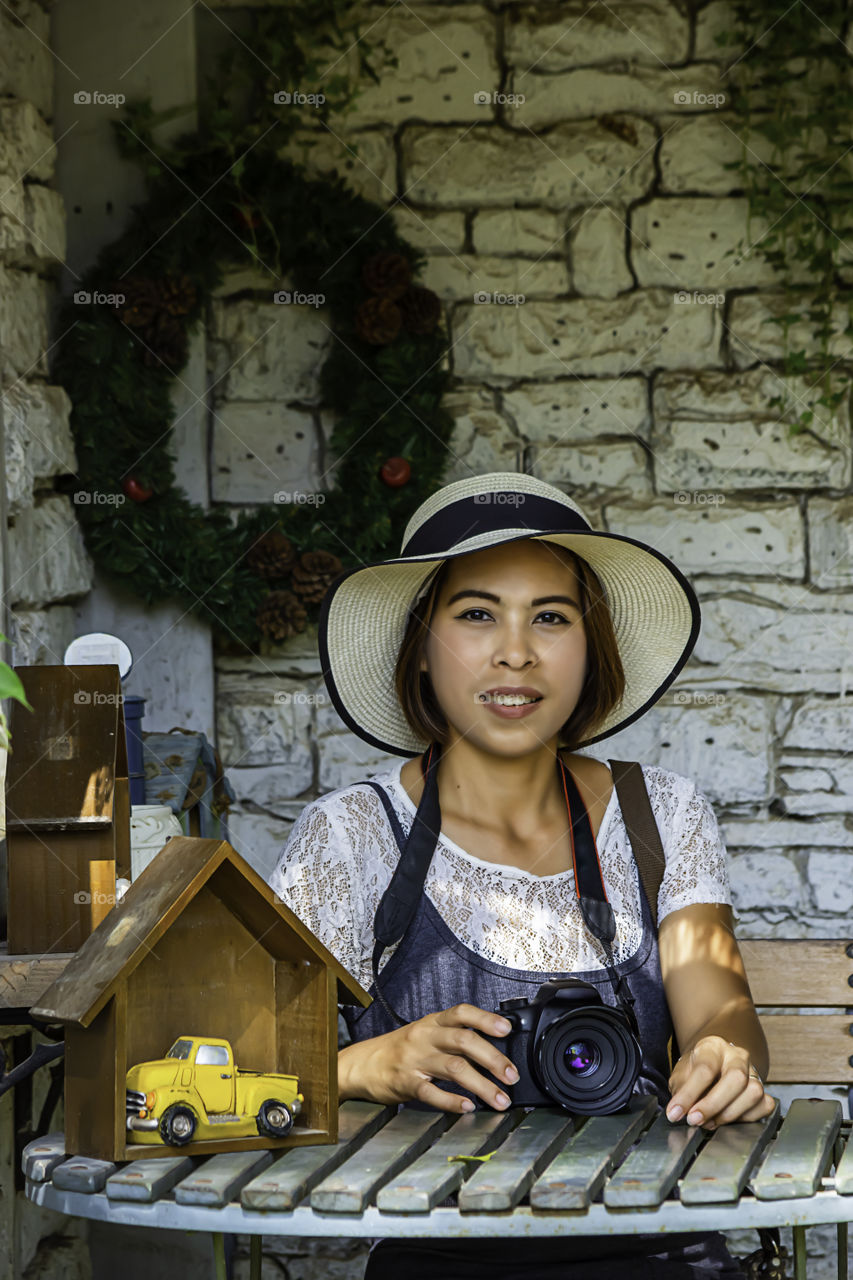 Asian woman with short hair wearing a hat and camera on the table background  white brick wall.