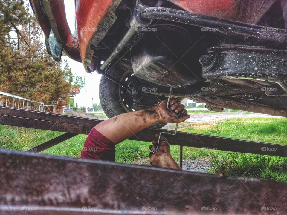 a man under the car with his hands and a metal key unscrews the bolts on the crankcase of a red car