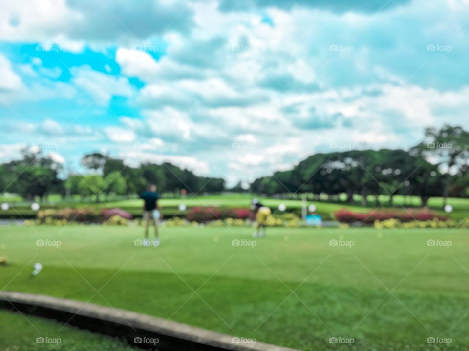 Blurred soft of two men are hitting golf on the golf course.