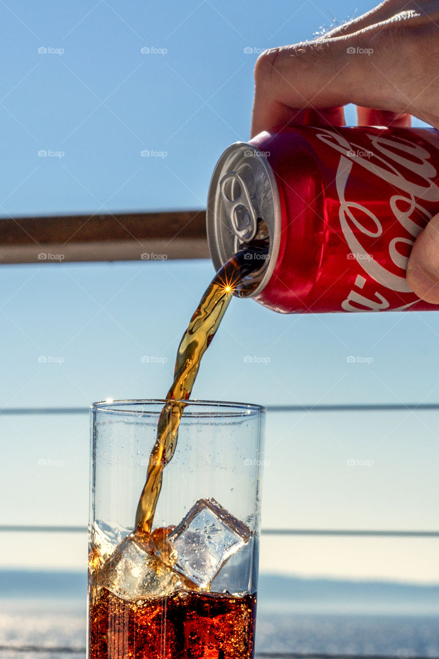 Pouring coke into glass full of ice cubes on sunny day. 