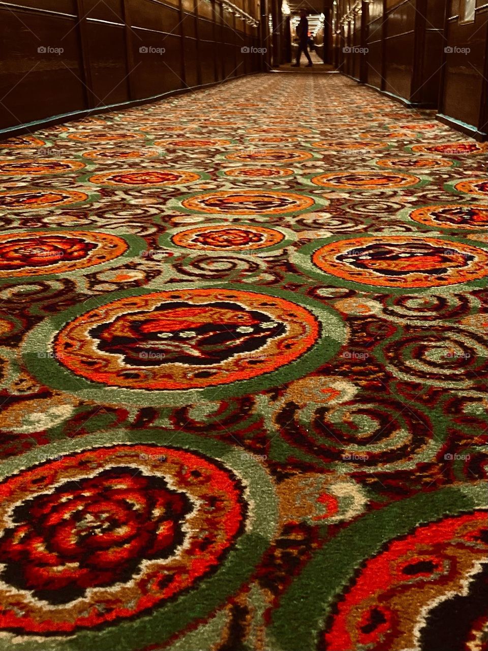 A red and green carpet running along a long hotel hallway conjuring nightmares from haunted hotels.