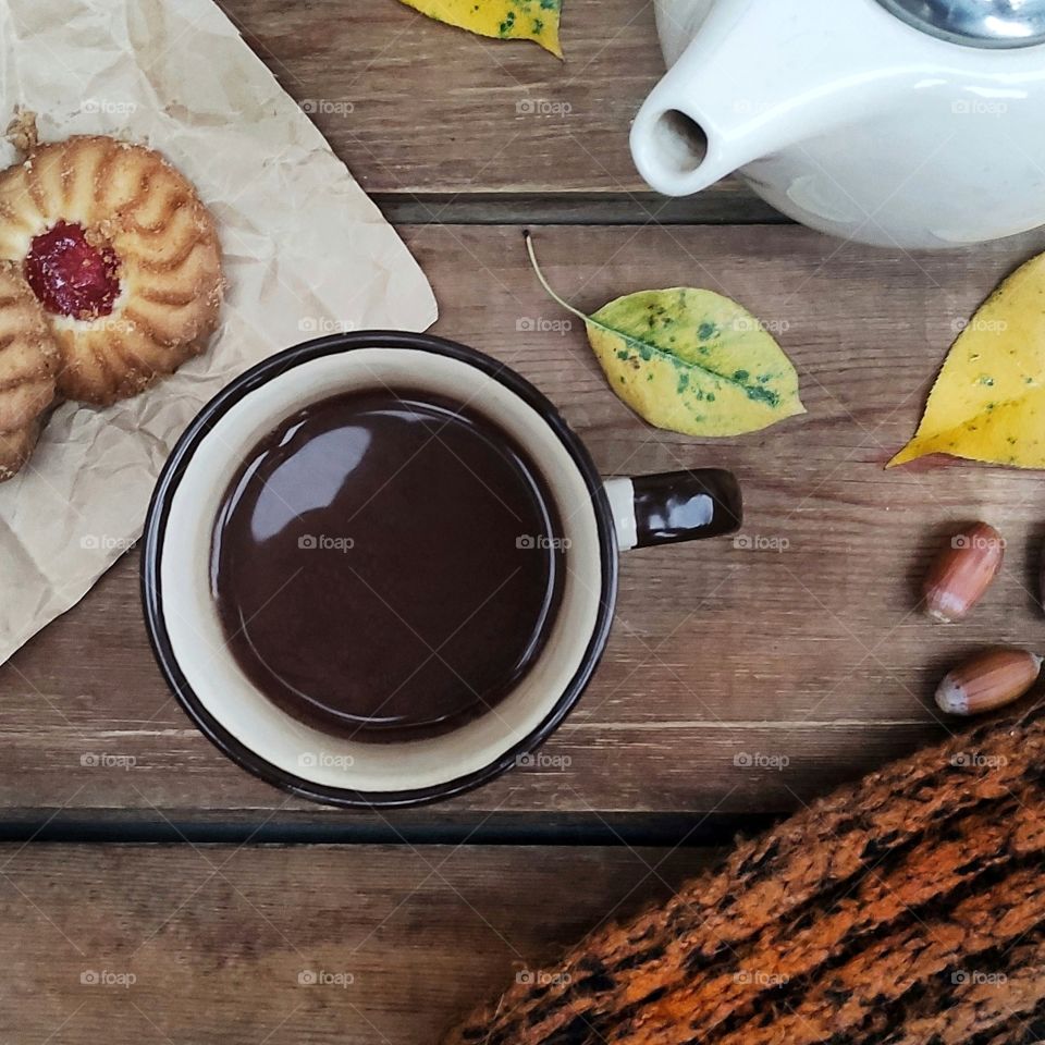 Hot scarf, yellow chocolate leaves and cookies on a wooden background in flat lay, autumn mood.