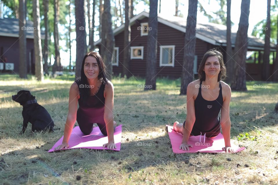 a girl in a black tracksuit, on a pink rug in the forest, does yoga, the girl meditates