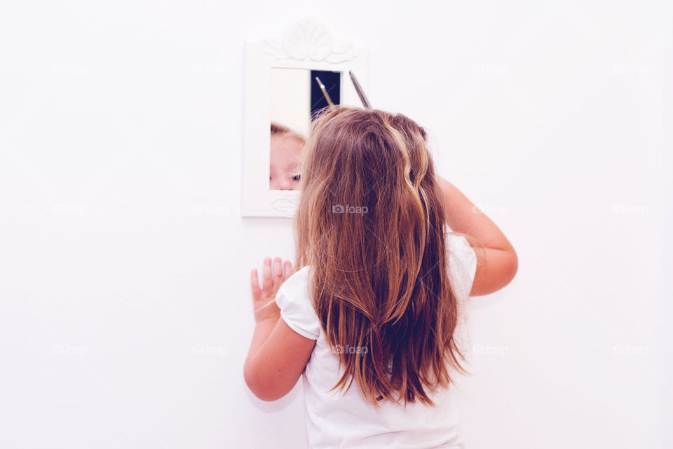 little girl cutting hair. little girl trying to cut her hair while looing in the mirror on the wall