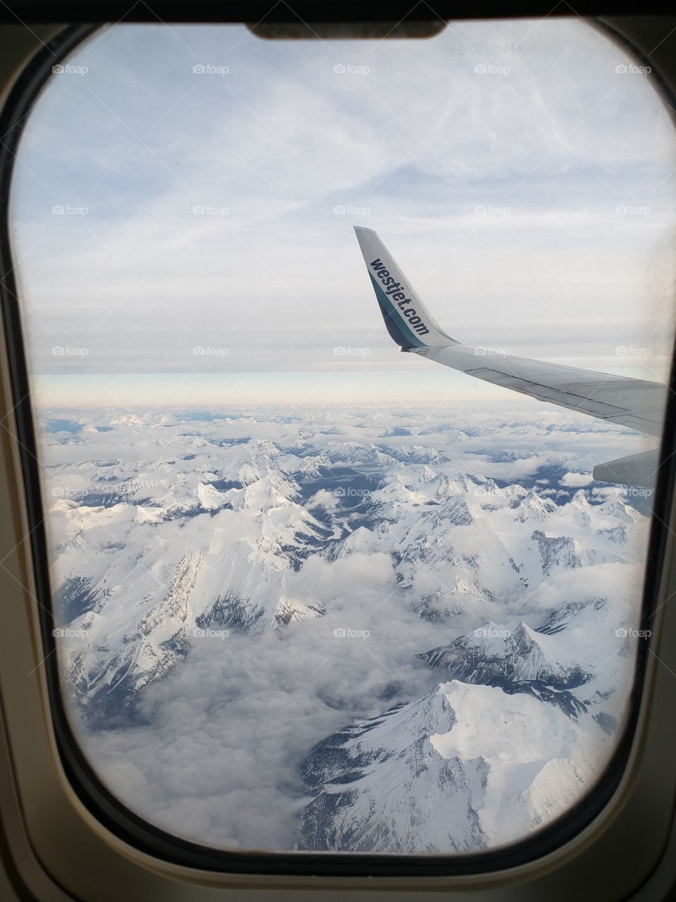 Airplane window view from Westjet flight travelling over the snowcapped Canadian Rockies Mountains