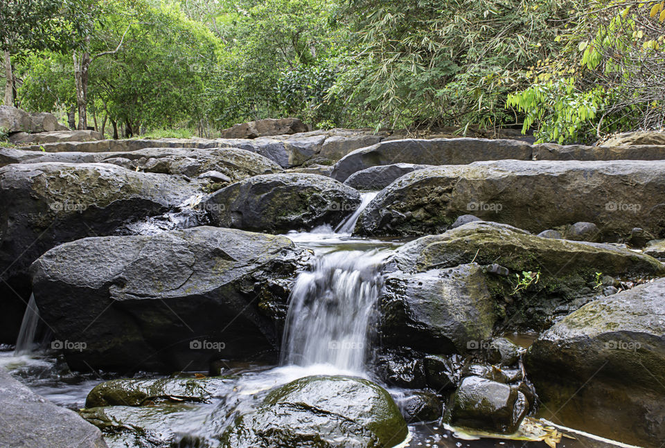 The water flowing over rocks and trees down a waterfall at Khao Ito waterfall , Prachin Buri in Thailand.