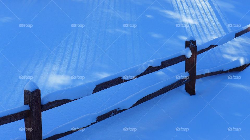 Winter wooden fence under snow and intriguing rays of sunlight