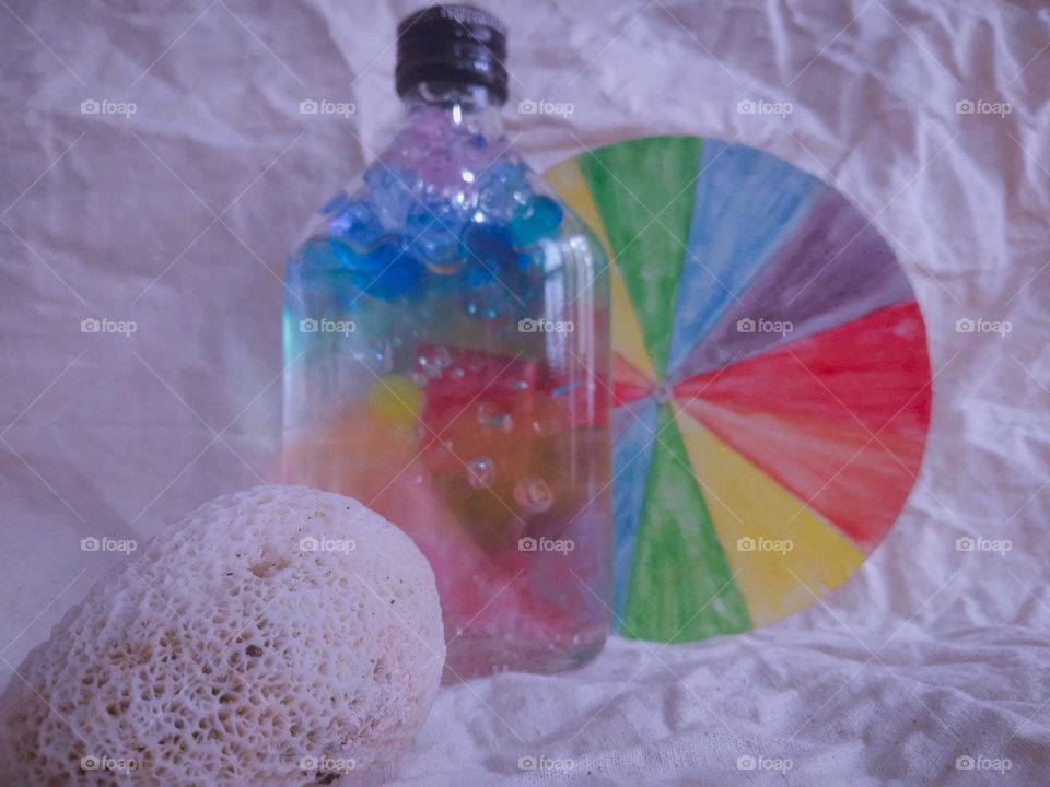 This is a colouful moment. There is a bottle with a full of colourful marbles.and also there is a colour plate behind the marble bottle. There is a sea shell  too. this is very creative idea..