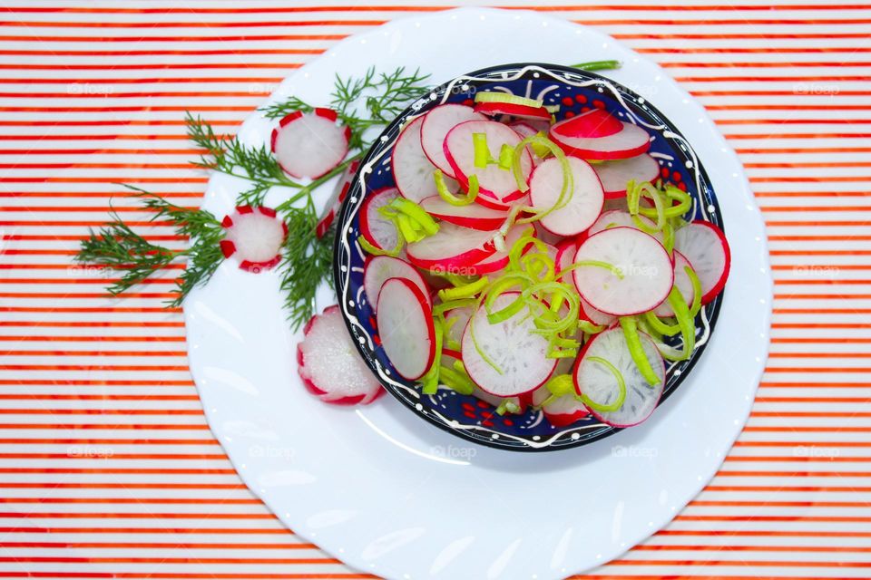 Fresh salad of radish, leek and dill in a bowl on a white red background.  Top view of food