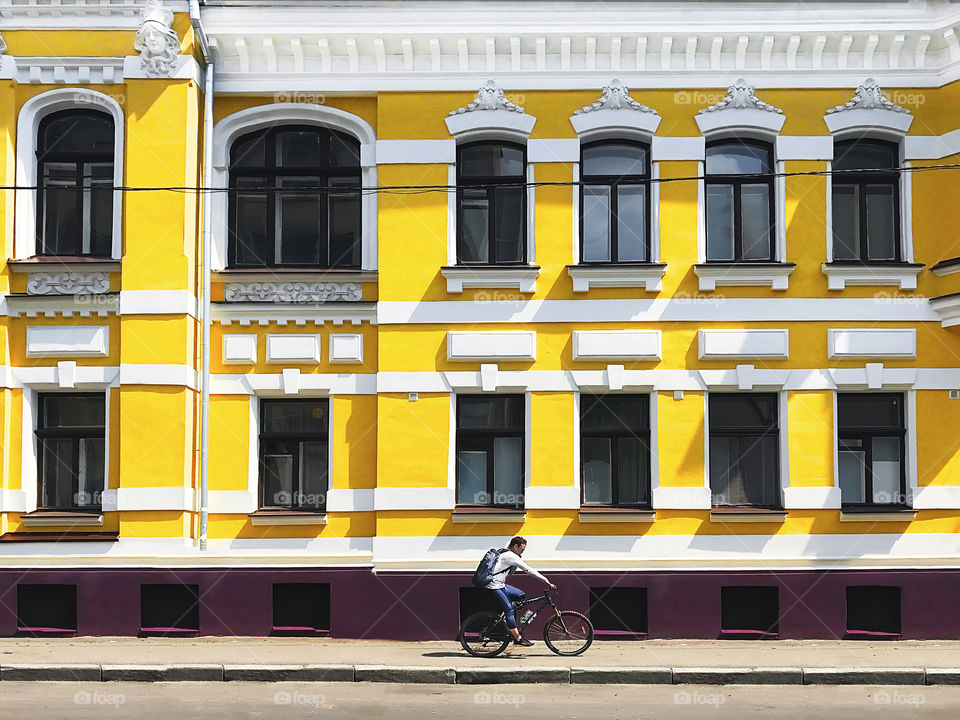 Young man riding a bicycle and using mobile phone in front of the old yellow building in the city 