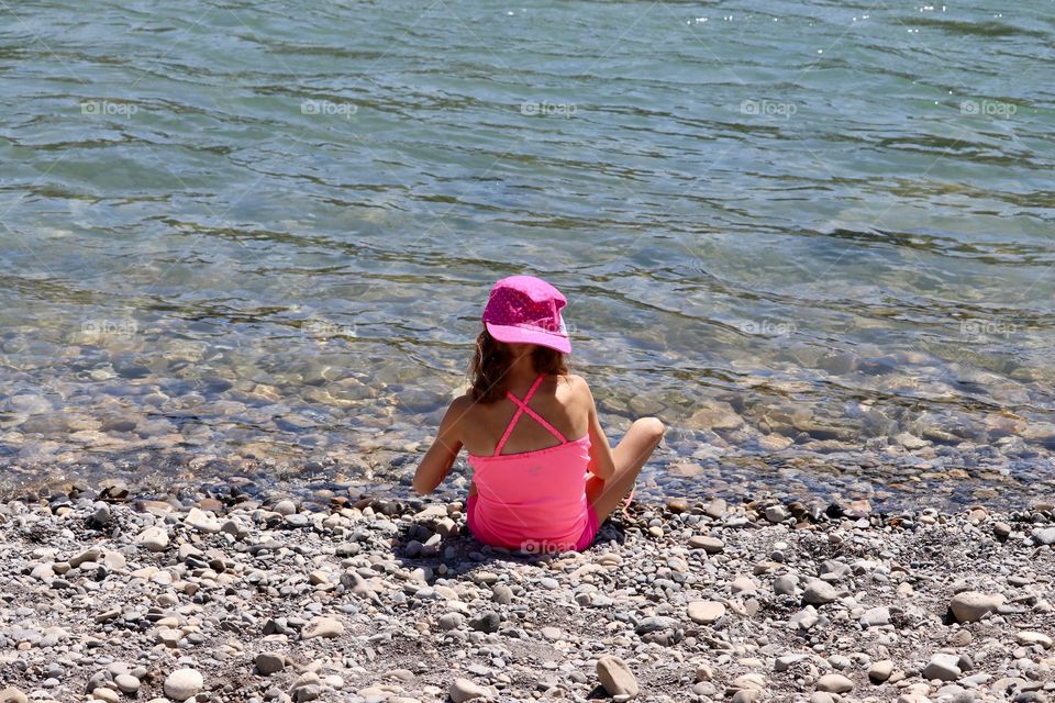 Little girl dressed all in pink sitting alone by herself beside river 