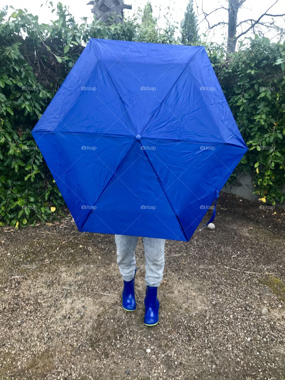 Child holding a blue umbrella and wearing blue rain boots in the rain 