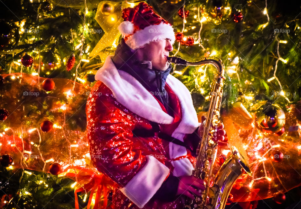 Cheerful Santa Claus Playing Saxophone Music In Front Of A Christmas Tree To Celebrate New Years Eve
