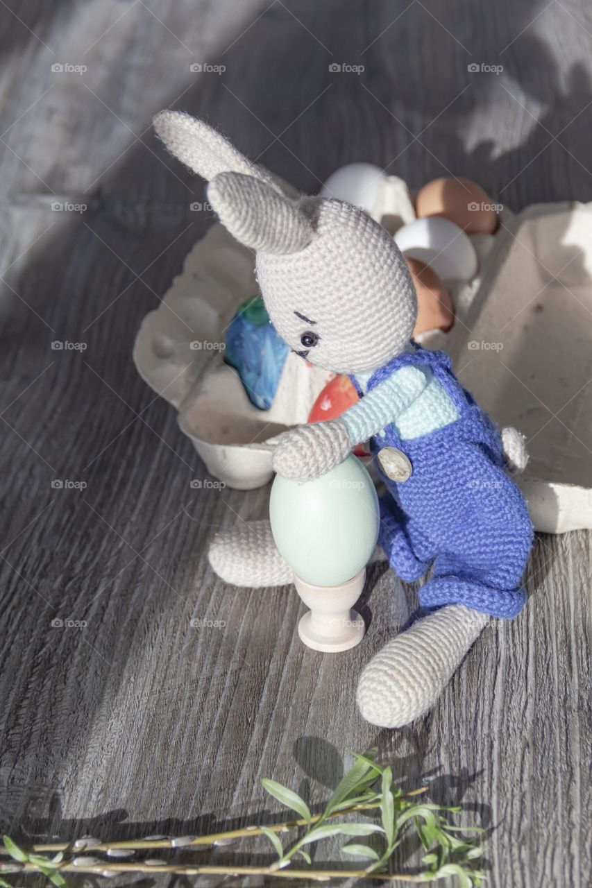 The rabbit of blue color is knitted by own hands at home.  Easter Bunny and chicken egg on coasters.  Craft product.