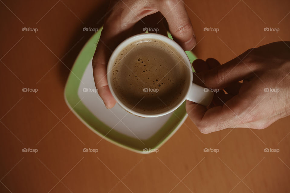 
Male hands holding cup of coffee on wooden table background.