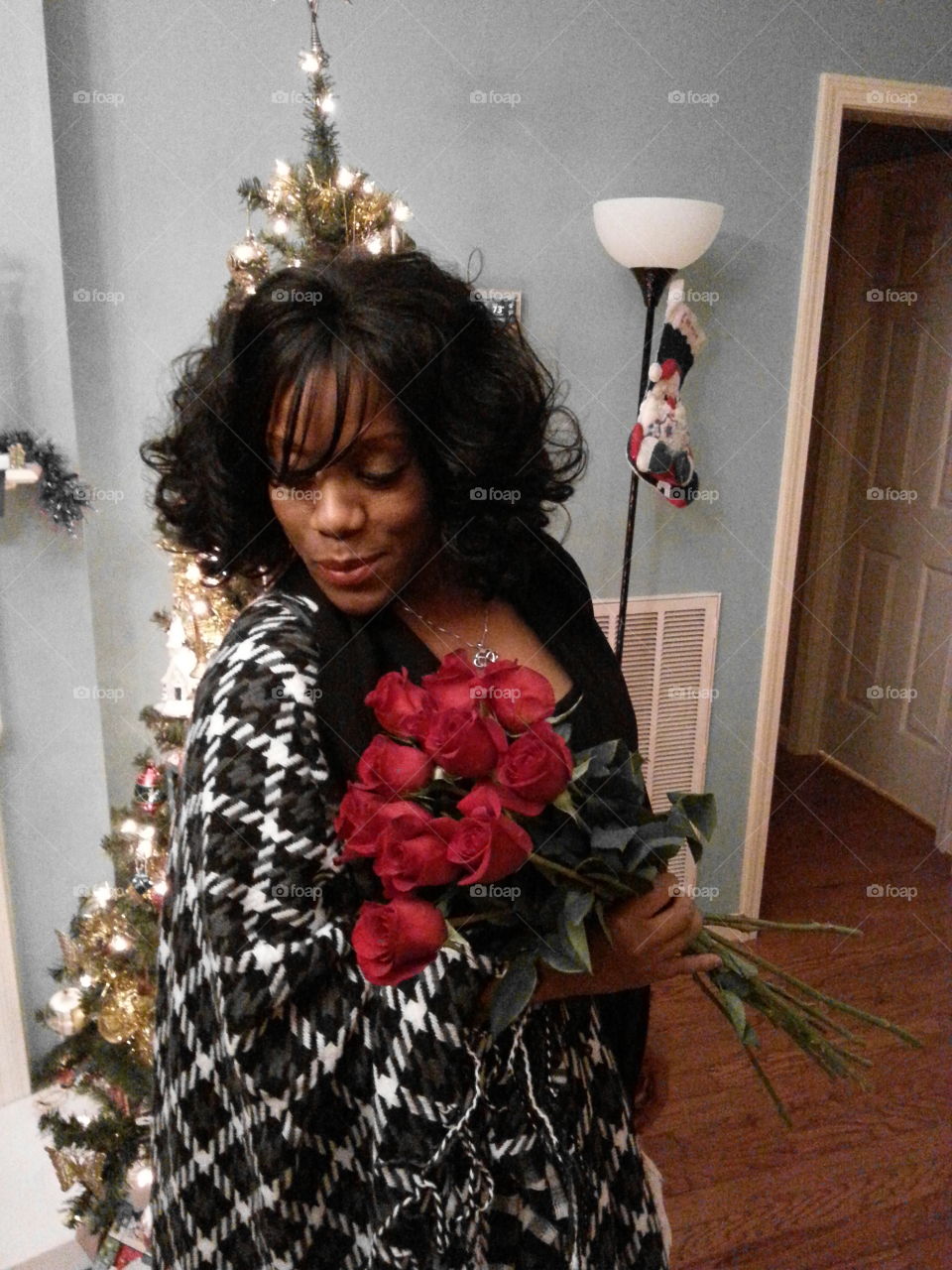 African woman standing in front of illuminated christmas tree with rose bouquet in hand