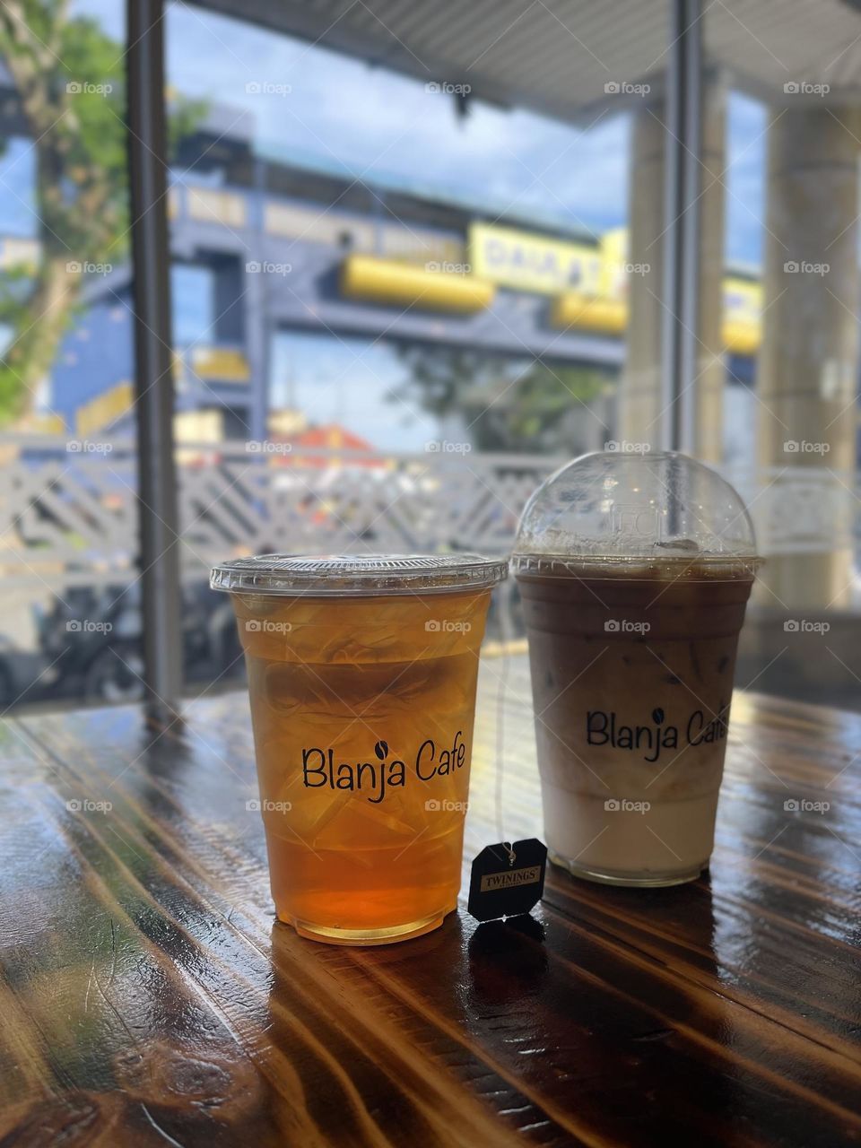 Close up view of two cups of drinks in a plastic container beside a beautiful scenery window 