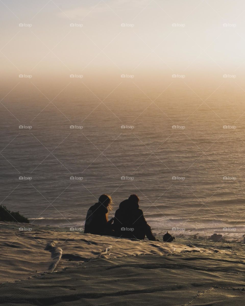 Two people meditating near the ocean witnessing a very beautiful sunset at the golden hour!