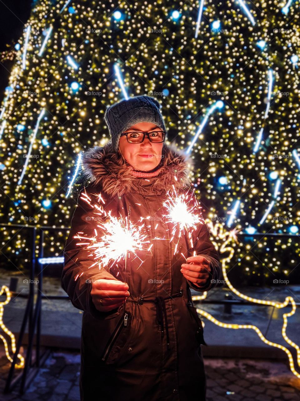 Young woman with sparkles in her hands standing in festive night city. Christmas,  New Year celebration