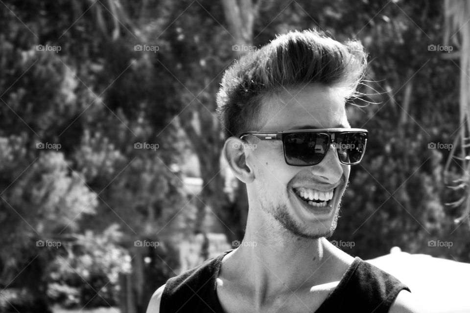 blonde 
man laughing at the beach wearing shades