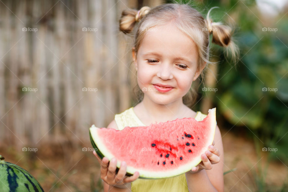Portrait of cute little girl with blonde hair which eating watermelon outdoor 