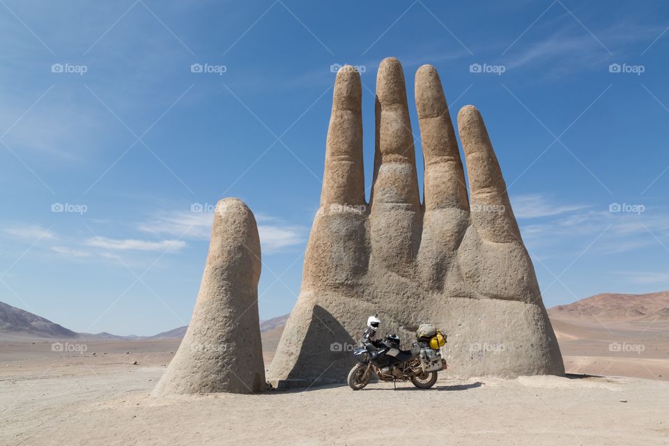 Hand of the desert. Mano del Desierto, hand of the desert statue in northern Chile. Clear blue sky. Few hills on the back ground. Motorcycle