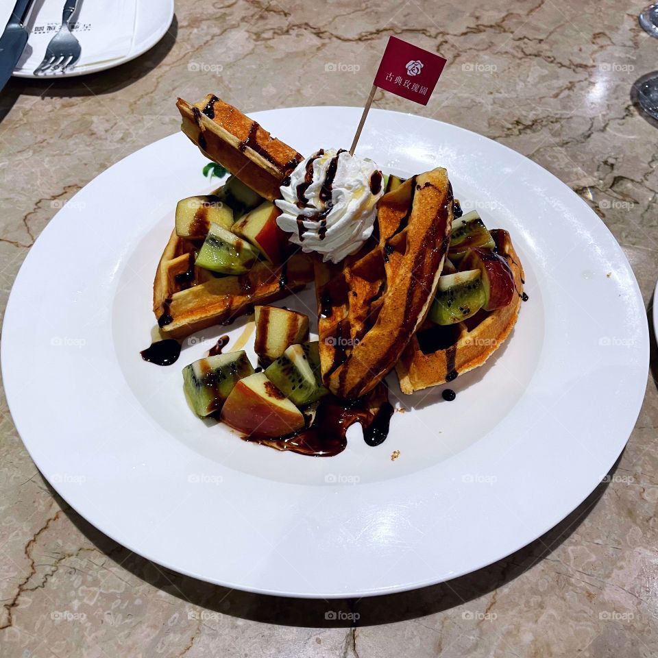 A plate of waffles with whipped cream and seasonal fruit. It is on a marble table. 