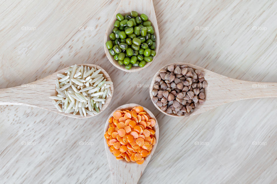 Four different grains in wooden spoons. Dal, moong beans, rice and buckwheat. Healthy eating concept, flatlay