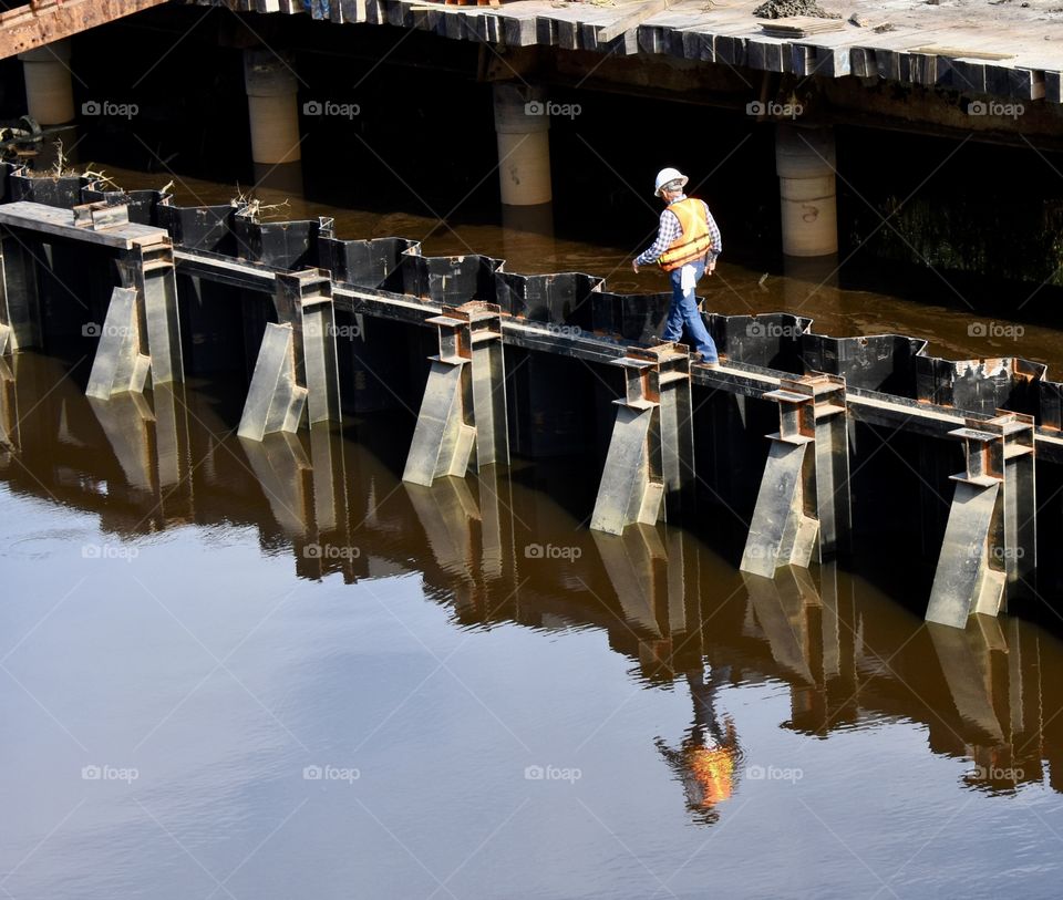 Construction worker walking reflecting into water 