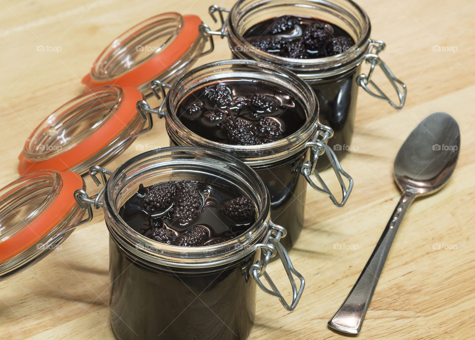 Three open jars of mulberry preserve with a spoon in a wooden background.