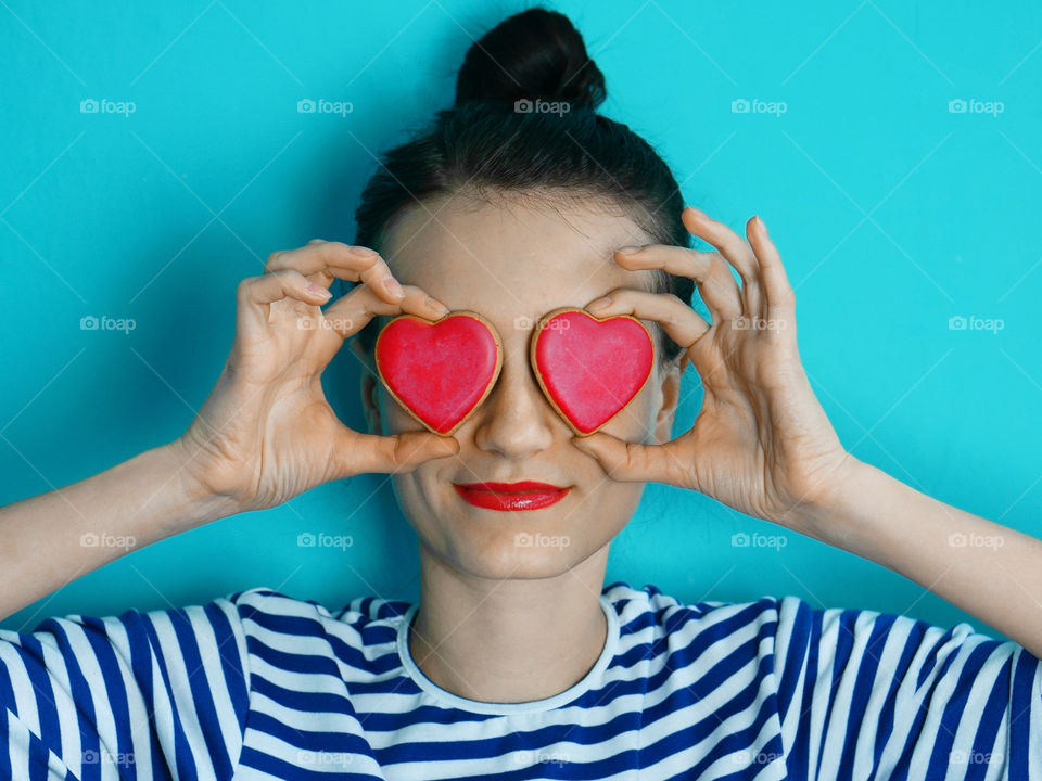 girl holding two heart shaped cookies against her eyes