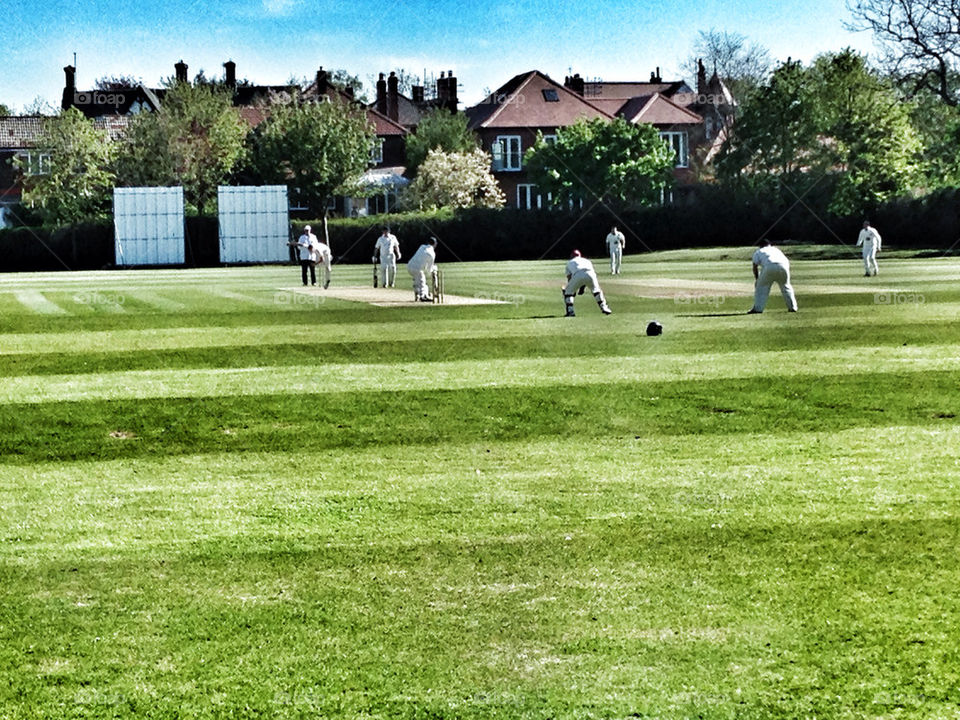 A GAME OF CRICKET IN PROGRESS IN AN ENGLISH TOWN WITH TYPICAL ENGLISH