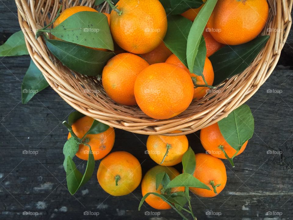 Wooden basket filled with mandarines and mandarine leaves on wooden table 