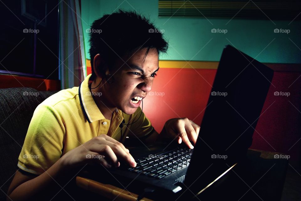 young asian teen intensely playing on a laptop computer