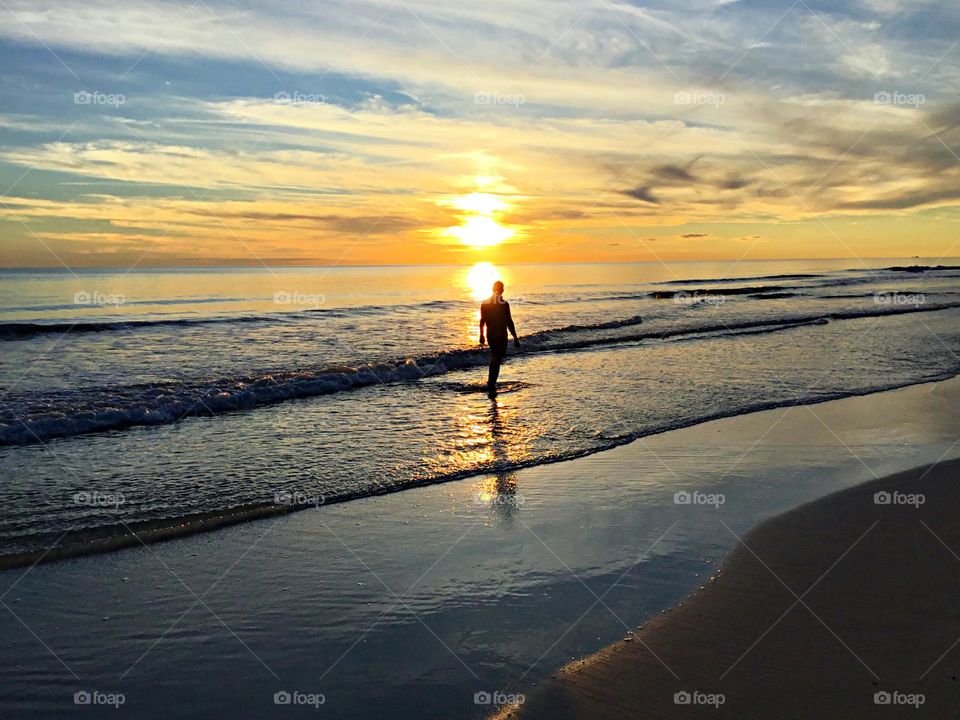 A silhouette of a man wading into the sunset in the Gulf of Mexico as it reflects off the waves