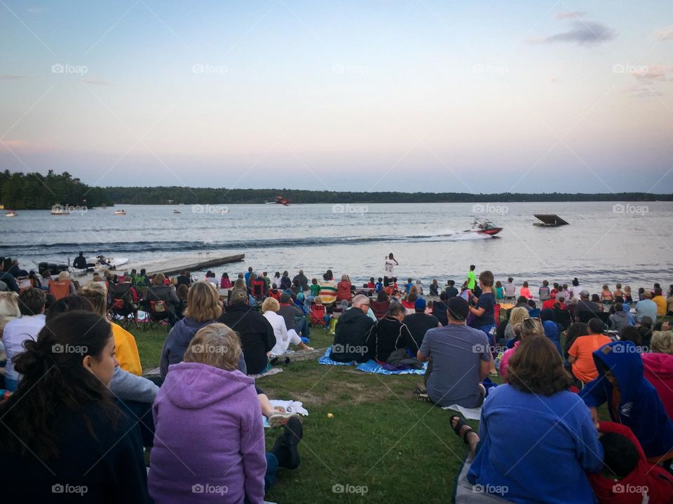 Crowd sitting on the grass watching a wakeboard show.