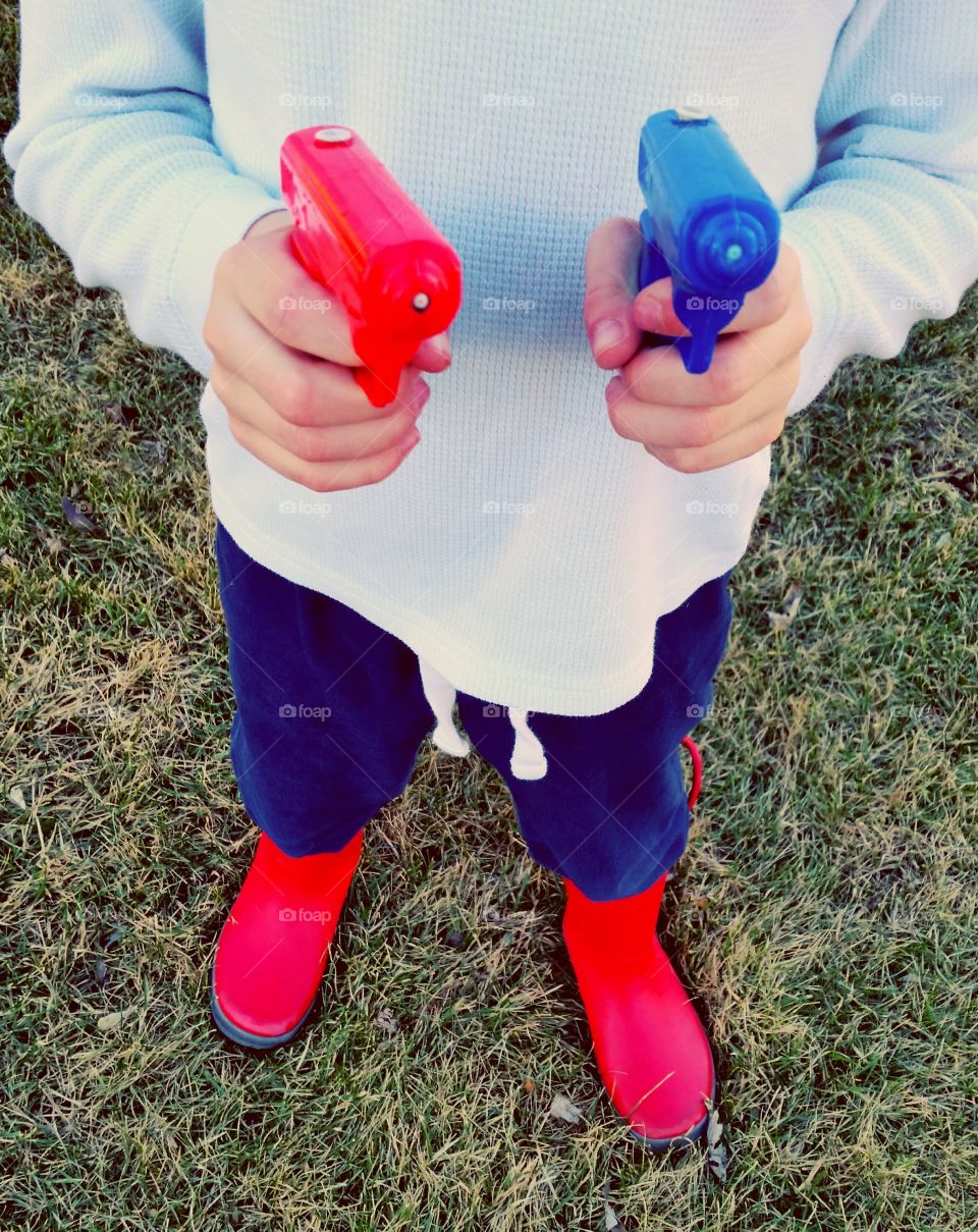 child holding red and blue squirt guns