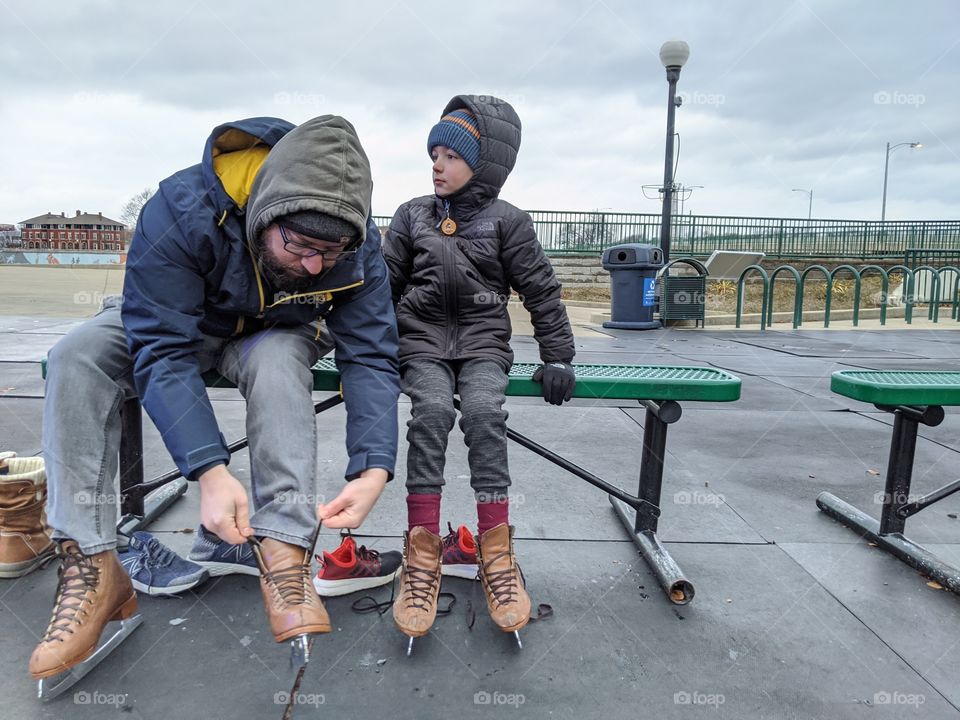 Father and son sitting on a bench in an urban setting outdoors during the winter while putting on ice skates