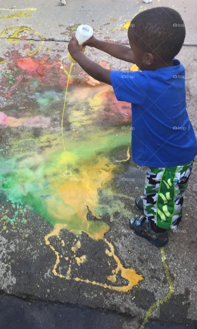 Boy painting with liquid paint on sidewalk
