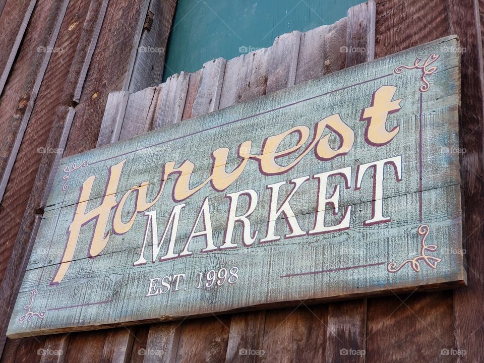 A sign for a farming harvest market made from weathered wood