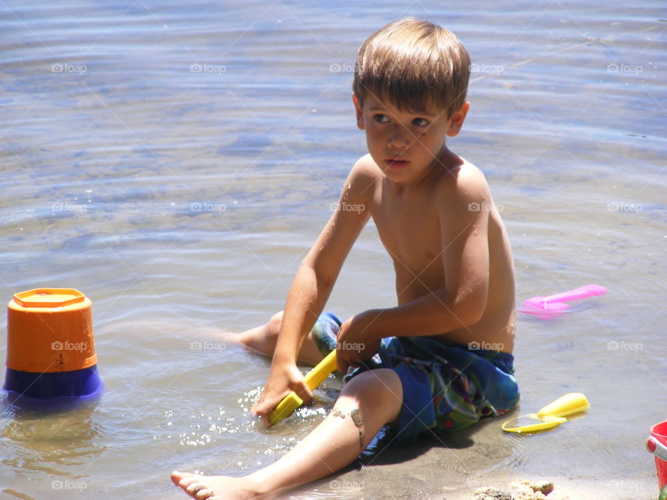 Young boy digging in the sand in the water