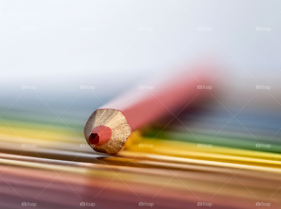 A portrait of a red colored pencil lying on the rest of the colorful pencils of a pencil box.