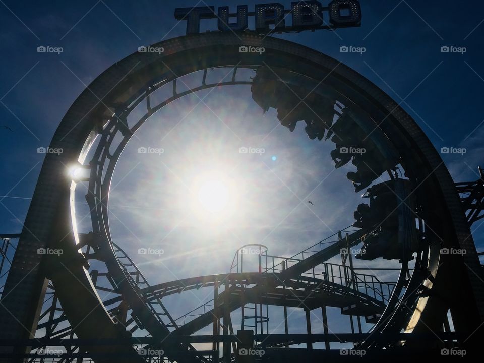 Turbo rollercoaster ride looping the loop on Palace Pier, Brighton, visited in Summer. Sun in background.